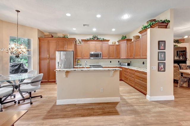 kitchen featuring light wood-type flooring, visible vents, an island with sink, stainless steel appliances, and an inviting chandelier