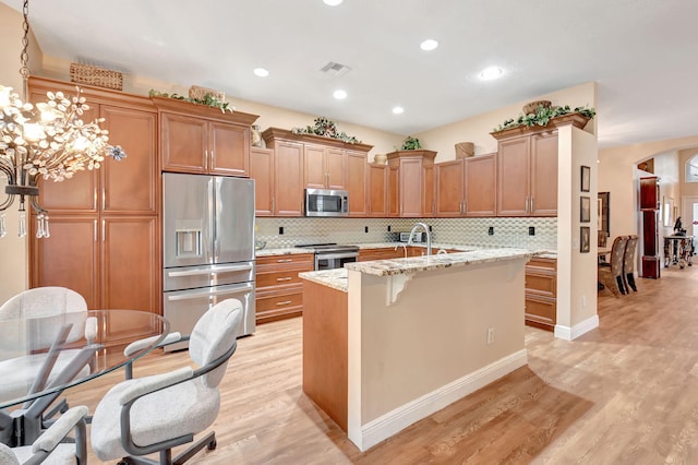 kitchen with light wood finished floors, visible vents, light stone countertops, an island with sink, and appliances with stainless steel finishes