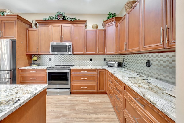 kitchen with backsplash, appliances with stainless steel finishes, light wood-type flooring, and light stone countertops