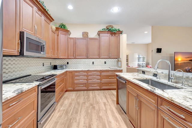 kitchen featuring light stone countertops, a sink, light wood-style floors, appliances with stainless steel finishes, and tasteful backsplash