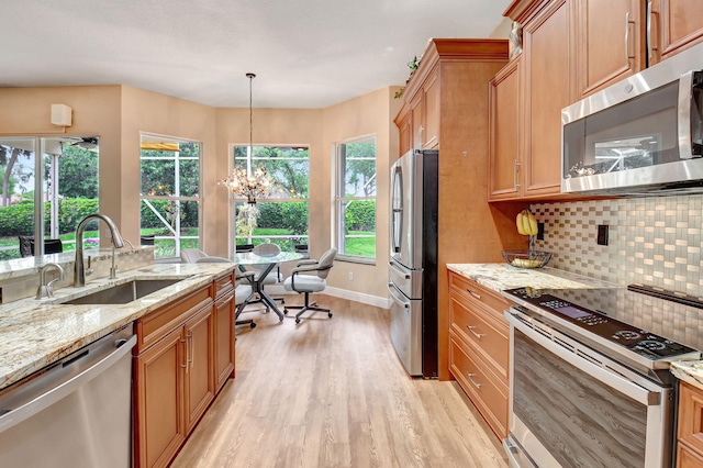 kitchen with light stone counters, light wood-style flooring, a sink, decorative backsplash, and appliances with stainless steel finishes