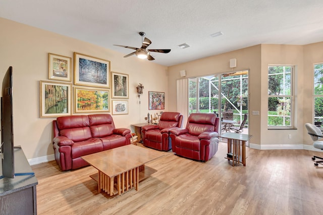 living area with light wood-style flooring, plenty of natural light, a ceiling fan, and baseboards