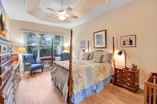 bedroom featuring light wood finished floors, a ceiling fan, a raised ceiling, and baseboards