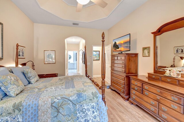 bedroom featuring visible vents, a tray ceiling, arched walkways, ceiling fan, and light wood-style floors