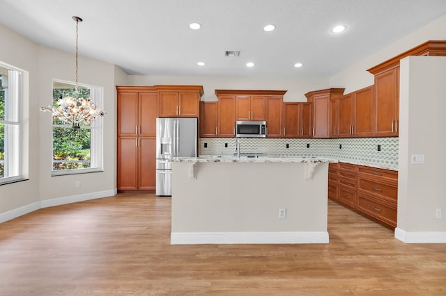 13594 Morocca Lake Ln, Delray Beach, FL 33446 - kitchen featuring appliances with stainless steel finishes, brown cabinets, a kitchen bar, a chandelier, and backsplash