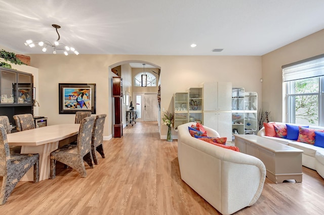 living room with light wood-style flooring, a notable chandelier, baseboards, and arched walkways