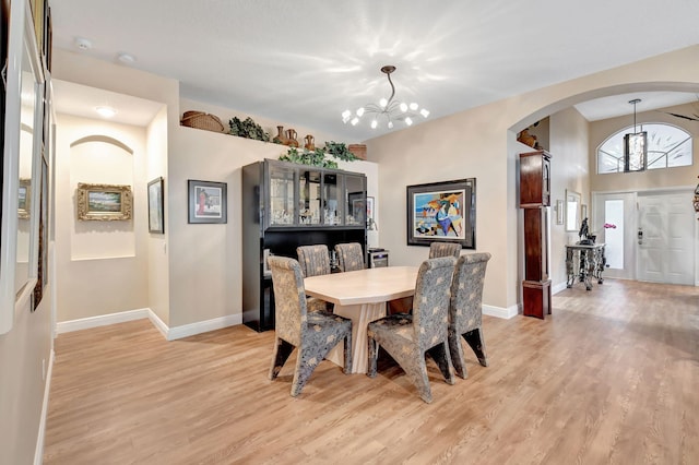 dining area featuring baseboards, arched walkways, a notable chandelier, and light wood finished floors