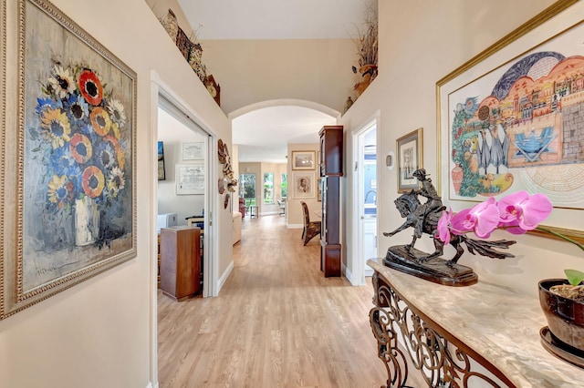 hallway featuring light wood-style floors, arched walkways, and baseboards