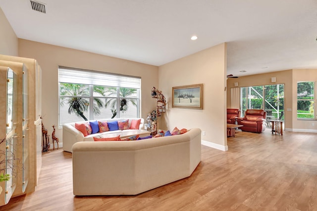 living room featuring light wood-style flooring, baseboards, visible vents, and a wealth of natural light