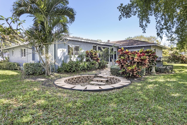 back of house featuring stucco siding, a lawn, and an outdoor fire pit
