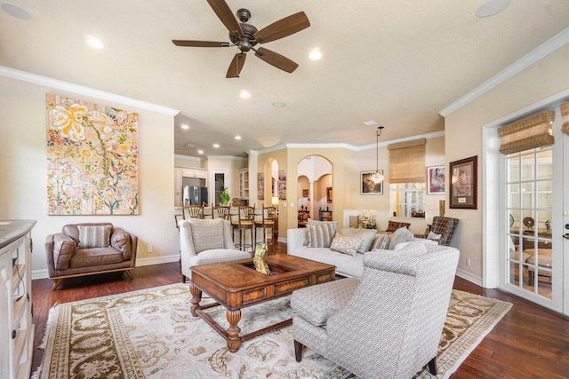 living area with arched walkways, crown molding, ceiling fan, baseboards, and dark wood-style floors