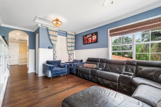 living room featuring ornamental molding, dark wood-style floors, arched walkways, wainscoting, and a textured ceiling
