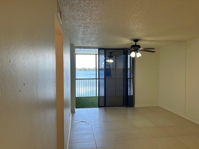 empty room with a wall of windows, ceiling fan, tile patterned flooring, and a textured ceiling