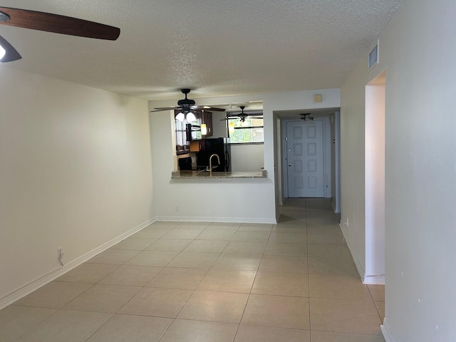 unfurnished living room with ceiling fan, a textured ceiling, visible vents, light tile patterned flooring, and baseboards