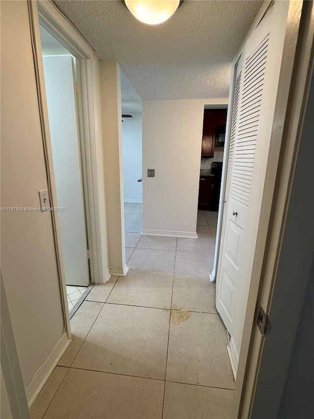 hall featuring a textured ceiling, light tile patterned floors, and baseboards