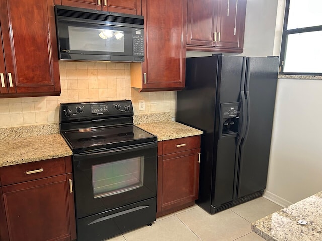 kitchen with light tile patterned floors, black appliances, light stone counters, reddish brown cabinets, and backsplash