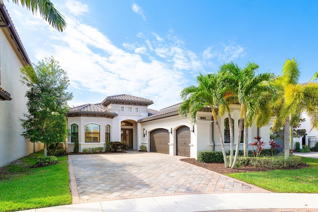 mediterranean / spanish house with a tiled roof, a front yard, stucco siding, decorative driveway, and a garage