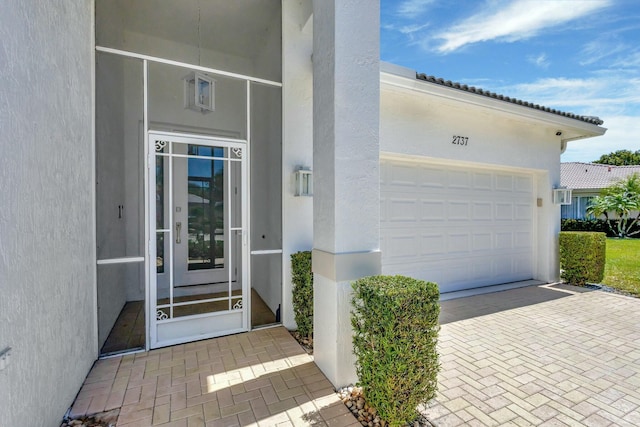2737 Clipper Cir, West Palm Beach, FL 33411 - doorway to property featuring stucco siding, decorative driveway, and a garage