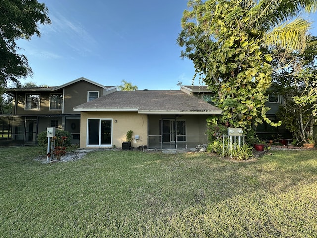 rear view of property with a shingled roof, a lawn, and stucco siding