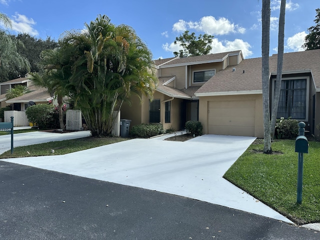 view of property with stucco siding, driveway, fence, a front yard, and a garage