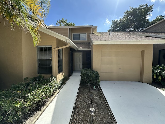 entrance to property featuring concrete driveway, an attached garage, and stucco siding