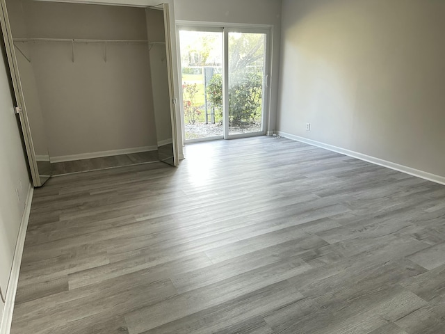 unfurnished bedroom featuring a closet, wood finished floors, baseboards, and access to outside