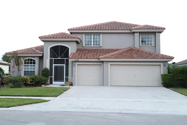 mediterranean / spanish-style home featuring driveway, stucco siding, a tiled roof, and a front lawn