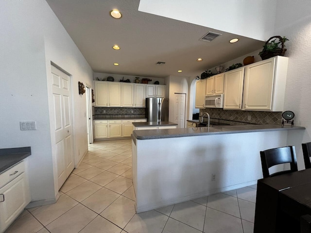 kitchen featuring white microwave, freestanding refrigerator, backsplash, recessed lighting, and dark countertops