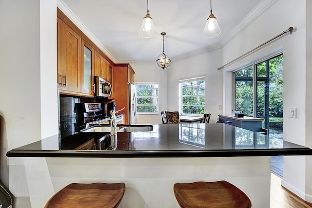 kitchen with a peninsula, ornamental molding, hanging light fixtures, appliances with stainless steel finishes, and brown cabinets