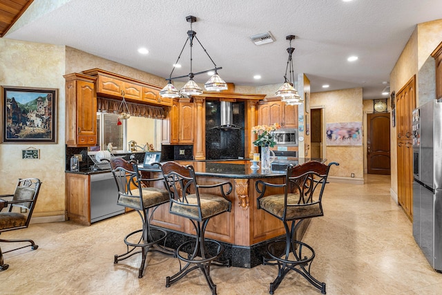 16090 Rio Del Paz, Delray Beach, FL 33446 - kitchen with appliances with stainless steel finishes, a kitchen island, brown cabinets, a kitchen bar, and wall chimney exhaust hood