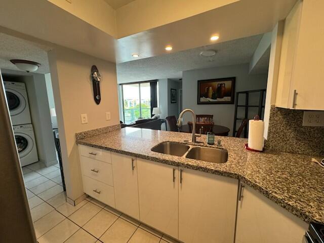 2075 SW 122nd Ave Unit 513, Miami, FL 33175 - kitchen featuring backsplash, a sink, stacked washer and clothes dryer, white cabinets, and dark stone counters