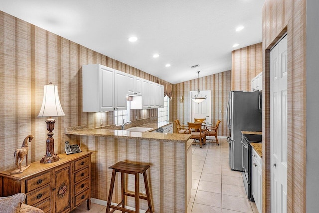 kitchen featuring a breakfast bar, a sink, range with electric stovetop, a peninsula, and wallpapered walls