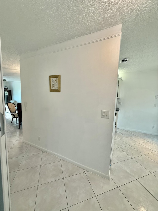 hall with light tile patterned floors, visible vents, a textured ceiling, and baseboards