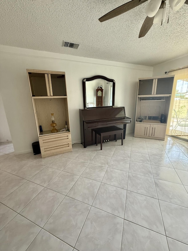 living area with tile patterned flooring, a textured ceiling, visible vents, and ceiling fan