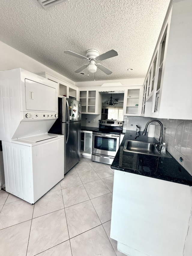 kitchen with a sink, white cabinetry, stacked washing maching and dryer, appliances with stainless steel finishes, and light tile patterned floors