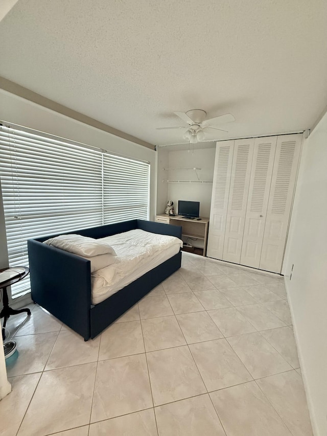 bedroom with baseboards, ceiling fan, light tile patterned floors, a closet, and a textured ceiling
