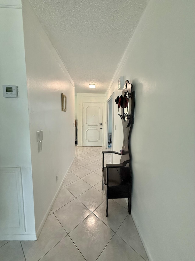 hallway featuring light tile patterned floors, baseboards, a textured ceiling, and crown molding