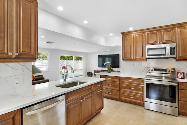 6611 NE 21st Ln, Fort Lauderdale, FL 33308 - kitchen featuring stainless steel appliances, a sink, light stone counters, a peninsula, and brown cabinets