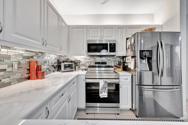 kitchen with light stone counters, backsplash, appliances with stainless steel finishes, and white cabinets