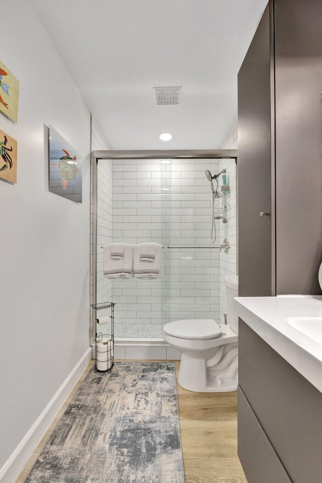 bathroom with toilet, wood finished floors, visible vents, and a stall shower