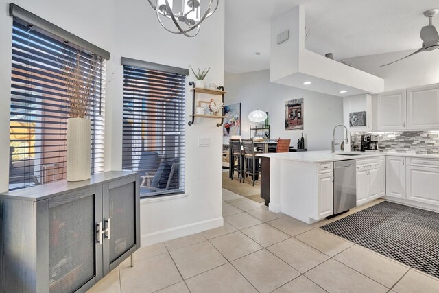 kitchen featuring a sink, stainless steel dishwasher, a peninsula, light tile patterned floors, and decorative backsplash