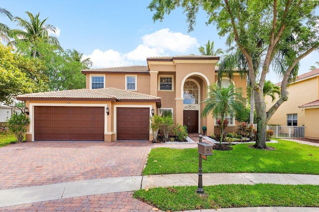 mediterranean / spanish-style home with a front lawn, stucco siding, an attached garage, a tile roof, and decorative driveway