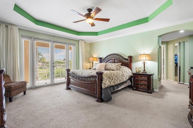 carpeted bedroom with crown molding, a textured ceiling, arched walkways, a tray ceiling, and access to outside