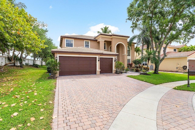 mediterranean / spanish-style home featuring stucco siding, an attached garage, a tiled roof, and a front yard
