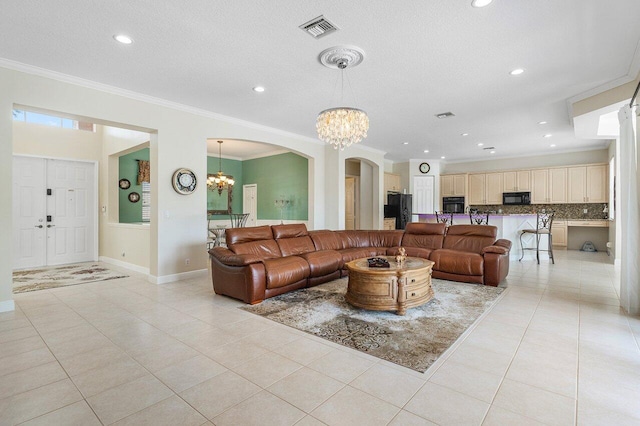 living room featuring visible vents, light tile patterned floors, arched walkways, crown molding, and a chandelier