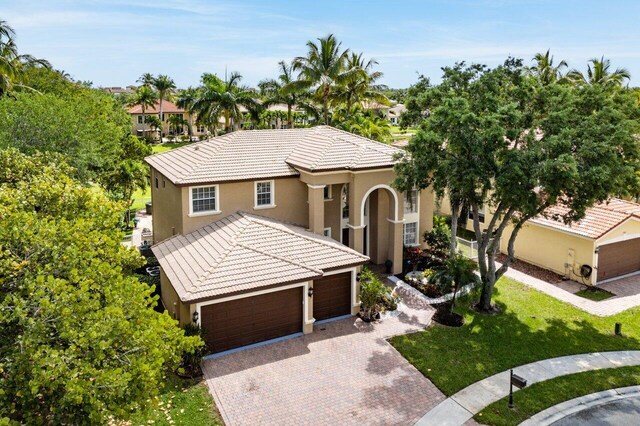 mediterranean / spanish home with a front lawn, a tiled roof, a garage, stucco siding, and decorative driveway
