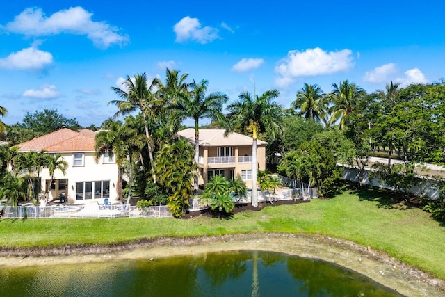 back of house with stucco siding, a water view, and a yard