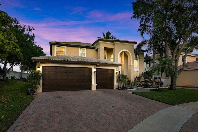 mediterranean / spanish-style home featuring a tiled roof, stucco siding, an attached garage, driveway, and a front yard