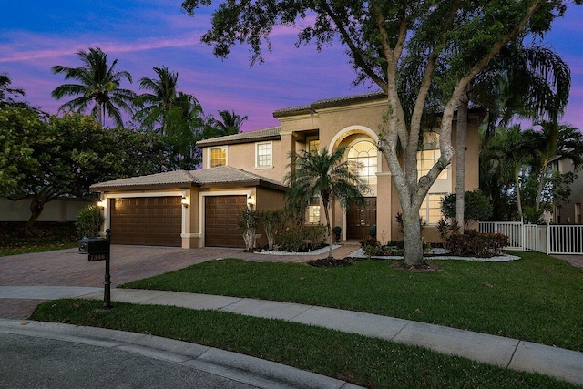 mediterranean / spanish house with fence, a tiled roof, stucco siding, decorative driveway, and a garage