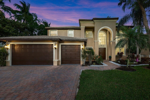 mediterranean / spanish home featuring a tile roof, a lawn, driveway, an attached garage, and stucco siding